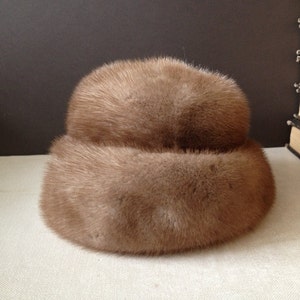 May include: A brown fur hat with a wide brim. The hat is made of soft, fluffy fur and has a simple, elegant design.