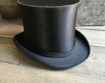 May include: A black top hat with a wide brim. The hat is made of a smooth, shiny material.