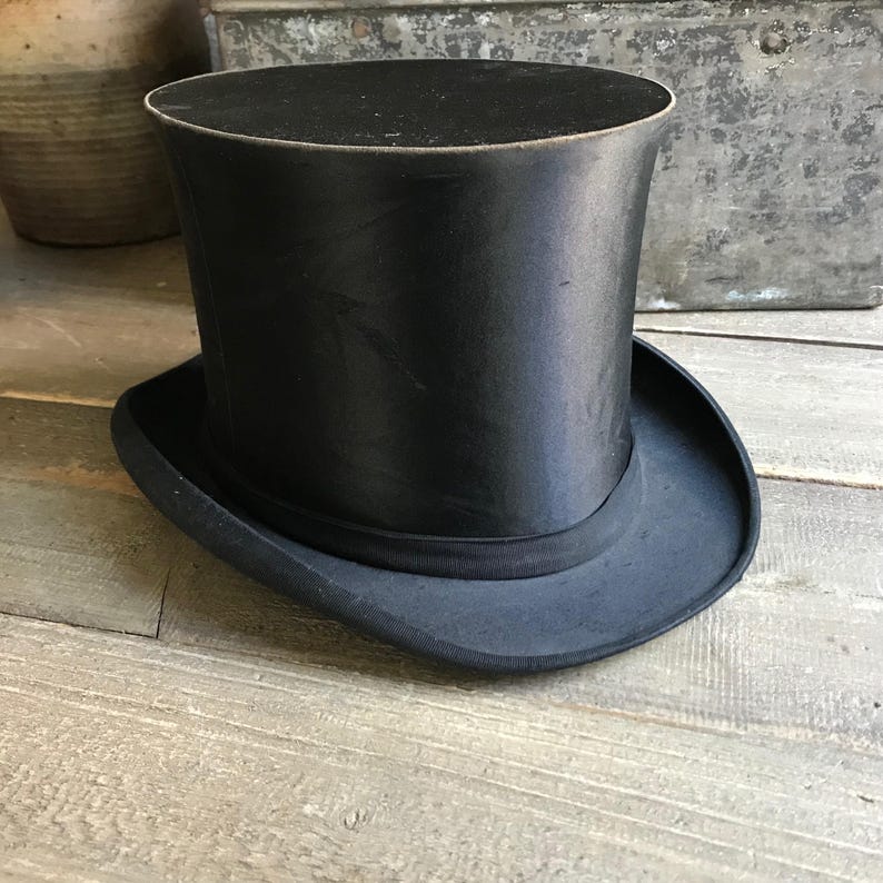 May include: A black top hat with a wide brim. The hat is made of a smooth, shiny material.