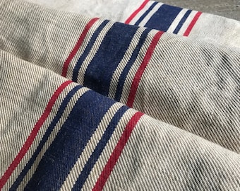 May include: Close-up of a fabric with a striped pattern in red, white, and blue. The fabric is woven with a subtle texture.