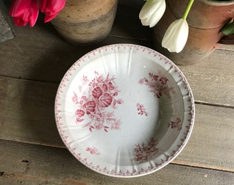 May include: A white ceramic bowl with a pink floral design. The bowl has a scalloped edge and a raised rim.