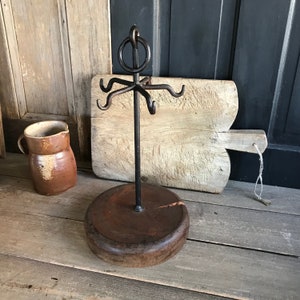 Puede incluir: Un soporte para utensilios de metal rústico con una base de madera y cinco ganchos. El soporte está hecho de metal negro y tiene un diseño simple. La base de madera es de color marrón oscuro y tiene un acabado natural.