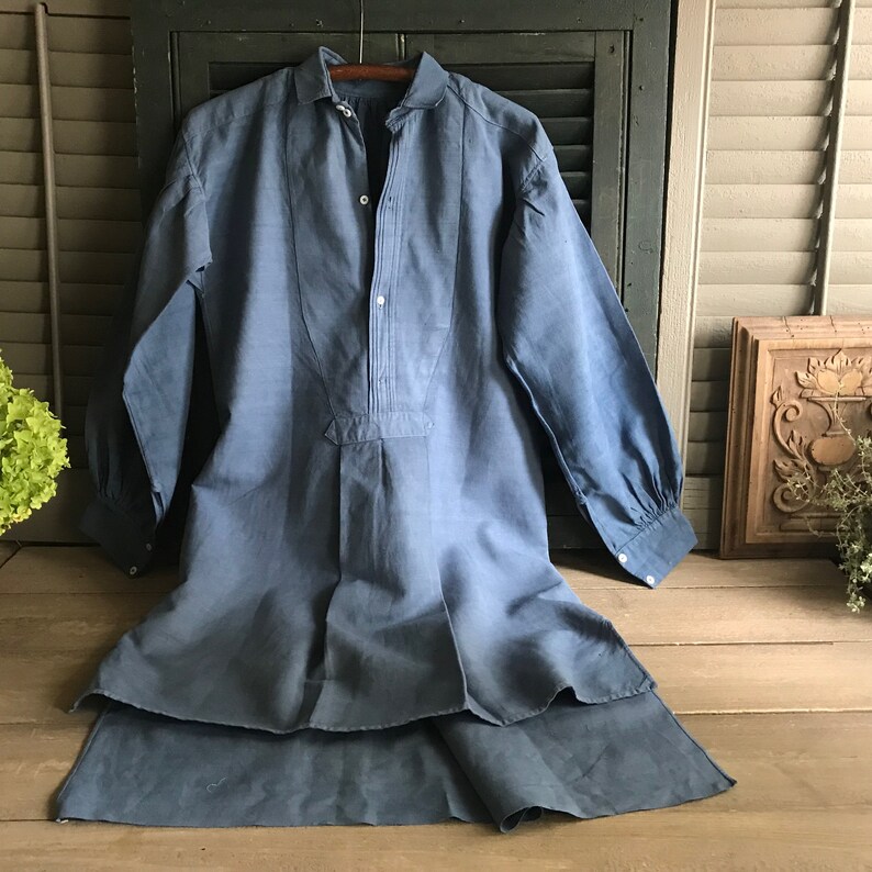 May include: A long-sleeved, blue linen shirt with a button-up front and a collar. The shirt has a pleated detail down the front and is made of a lightweight fabric.