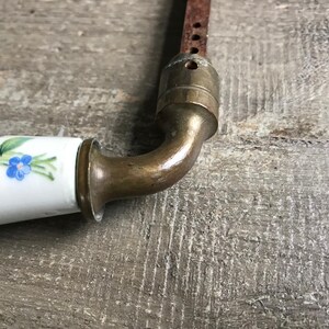 May include: A vintage porcelain door knob with a floral design. The knob is white with blue and green flowers. The metal part of the knob is brass.