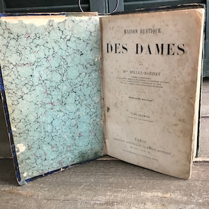 May include: A vintage book titled "Maison Rustique Des Dames" by M. Millet-Robinnet. The book is bound in blue and has a marbled paper cover. The title page is in French and includes the text "Tome Premier" and "Paris, Librairie Agricole de la Maison Rustique."