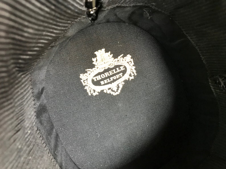 May include: The inside of a black hat with a white label that reads "THORELLE BELFORT".