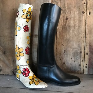 Op de afbeelding: Twee hoge laarzen, een met een witte basis en een geel en rood bloemenpatroon, de andere van zwart leer.