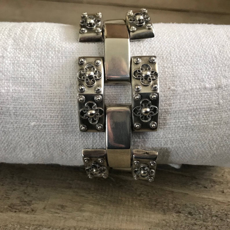 May include: A silver bracelet with a chain link design. Each link is decorated with a small flower-shaped design.