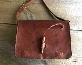 Puede incluir: Un bolso de cuero marrón con una correa de cuero trenzada y un cierre de madera.
