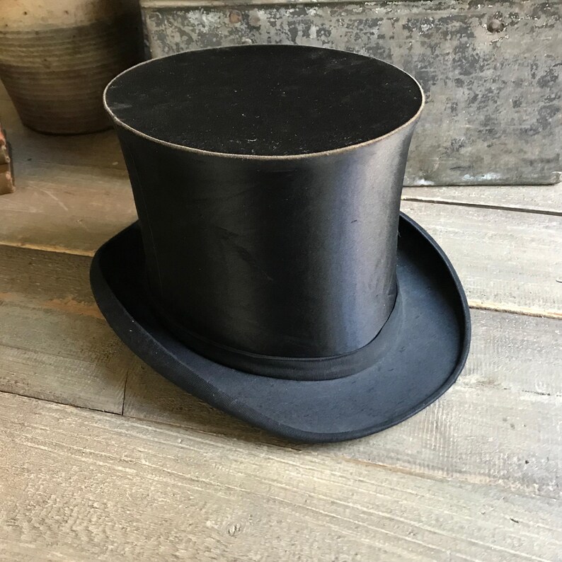May include: A black top hat with a wide brim. The hat is made of a smooth, shiny material.