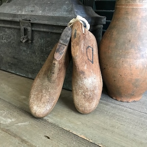 May include: Two wooden shoe lasts, one with a D carved into it, are sitting on a wooden surface. The lasts are a light brown color and have a rough texture.