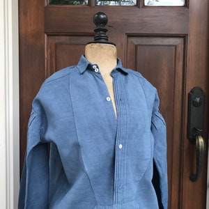 May include: A blue linen shirt with a button-up front and long sleeves. The shirt has a pleated detail down the front.