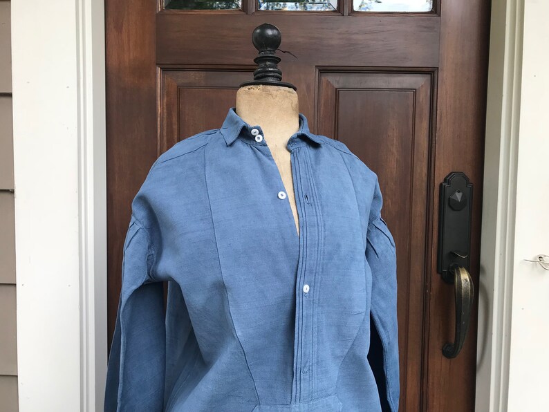 May include: A blue linen shirt with a button-up front and long sleeves. The shirt has a pleated detail down the front.