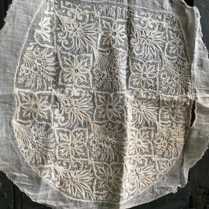 以下が含まれることがあります： 複雑な白い刺繍の円形デザインが施された白い綿の生地。刺繍は、花柄と幾何学模様の繰り返しパターンを特徴としています。