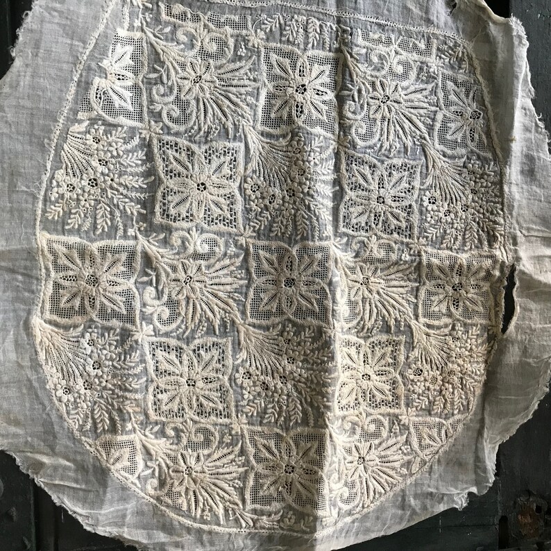 以下が含まれることがあります： 複雑な白い刺繍の円形デザインが施された白い綿の生地。刺繍は、花柄と幾何学模様の繰り返しパターンを特徴としています。