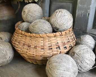 May include: A rustic, woven basket filled with several gray yarn balls. The basket is made of light brown wood and sits on a weathered wooden surface. Additional yarn balls are scattered around the basket, creating a cozy, craft-focused scene.