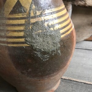 May include: A brown ceramic pitcher with gold stripes and a rough, textured surface. The pitcher has a wide base and a narrow neck.