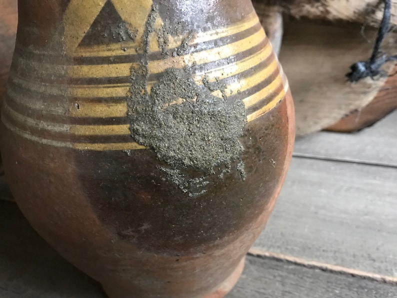 May include: A brown ceramic pitcher with gold stripes and a rough, textured surface. The pitcher has a wide base and a narrow neck.