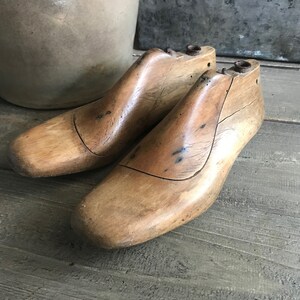 May include: A pair of vintage wooden shoe lasts, used by shoemakers to create custom footwear. The lasts are made of light brown wood and have a worn, rustic appearance.