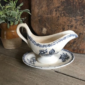 Könnte beinhalten: Eine weiße Porzellansauce mit einem blauen und weißen Blumenmuster. Die Sauce hat einen Griff und einen Sockel. Sie steht auf einer passenden Untertasse.