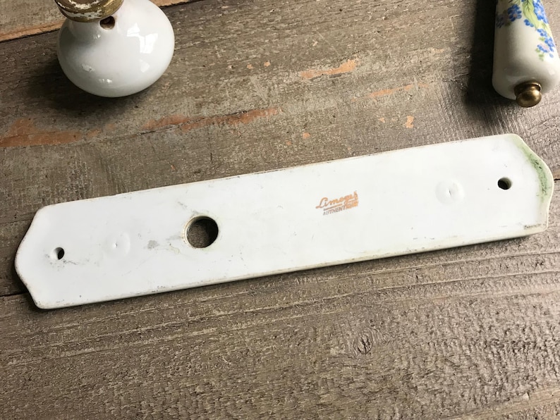May include: White porcelain door hardware with a round hole and three smaller holes. The backplate has the text "Limoges France" printed on it.