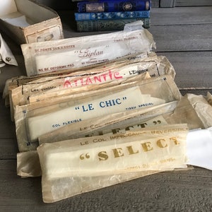 May include: A stack of vintage packaging for men's shirts. The packaging is made of paper and has a variety of colors and designs. The text on the packaging includes the words "Biplan", "Atlantic", "Le Chic", "Select", and "Tissu Special".