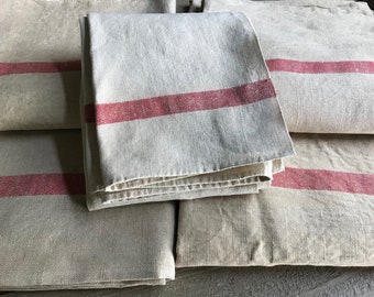 May include: A stack of five off-white linen tea towels with a single red stripe across the centre of each towel.