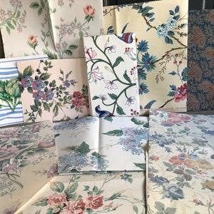 May include: Assortment of vintage floral wallpaper samples in various patterns and colors, including blue, pink, and green. The samples are arranged on a table and some have the text "RESTORATION KENANS" printed on them.