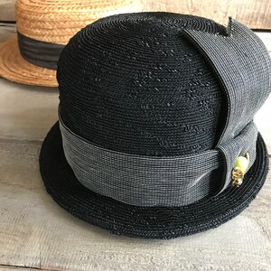 May include: A black straw hat with a wide brim and a gray ribbon. The hat has a decorative detail on the side.