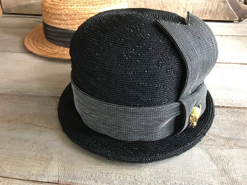 May include: A black straw hat with a wide brim and a gray ribbon. The hat has a decorative detail on the side.
