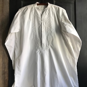 May include: A white long-sleeved shirt with a mandarin collar and a button-up front. The shirt has decorative stitching on the front and is made of a lightweight fabric.
