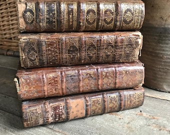 May include: A stack of four antique leather-bound books with gold accents and ornate designs. The books are worn and have a vintage aesthetic.