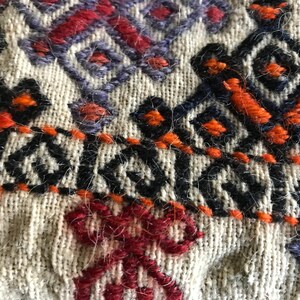 May include: Close-up of a woven fabric with intricate embroidery in shades of orange, red, black, and purple. The fabric has a textured, fuzzy surface.