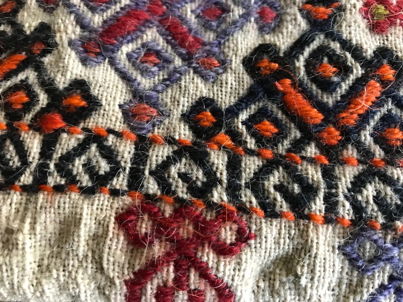 May include: Close-up of a woven fabric with intricate embroidery in shades of orange, red, black, and purple. The fabric has a textured, fuzzy surface.