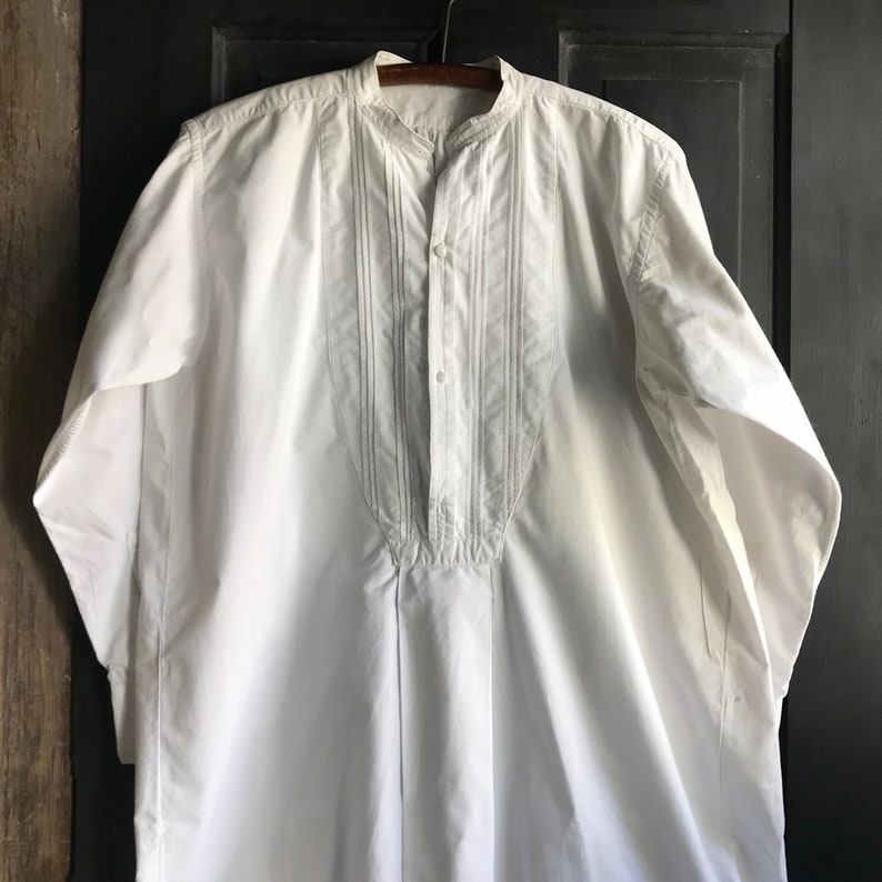 May include: A white long-sleeved shirt with a mandarin collar and a button-up front. The shirt has decorative stitching on the front.