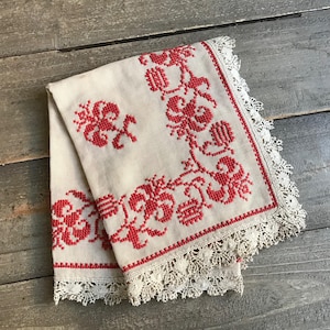 May include: A white linen tablecloth with red embroidered floral designs and a lace border.
