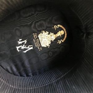 May include: The inside of a black hat with a gold label that reads "Teil-Mellet & Co.  -  Auteurs & Fabricants -  BELGIUM" and the number "114" in white.