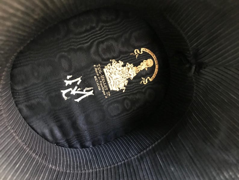 May include: The inside of a black hat with a gold label that reads "Teil-Mellet & Co.  -  Auteurs & Fabricants -  BELGIUM" and the number "114" in white.