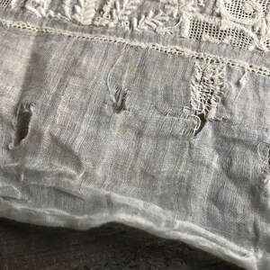 以下が含まれることがあります： 白い布のクローズアップ。いくつかの穴と繊細な刺繍模様があります。布は古びていて、ビンテージな外観をしています。