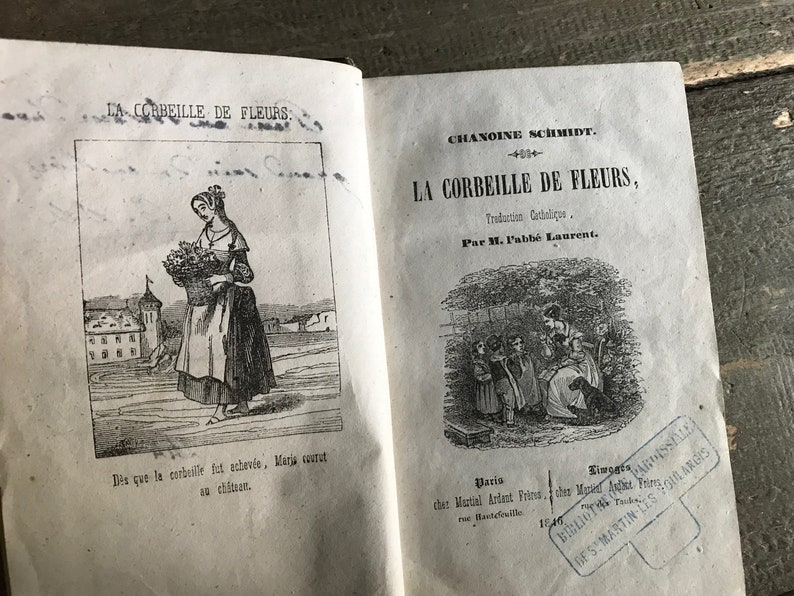 May include: A vintage book titled "La Corbeille de Fleurs" by Chanoine Schmidt. The book cover features a black and white illustration of a woman carrying a basket of flowers. The book is published by Martial Ardant Fr&egrave;res in Paris and Limoges.