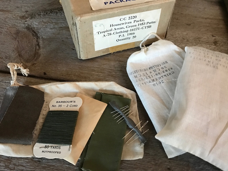 May include: A set of sewing supplies in a white cloth bag. The supplies include a spool of green thread labeled "Barbour's No. 35 - 2 Cord", a small piece of green fabric, a small piece of brown fabric, a small piece of beige fabric, a small metal needle holder with needles, and a small white tag that says "50-yards rotproofed".
