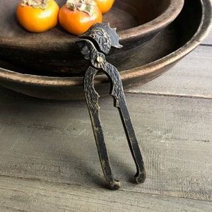 May include: Black metal nutcracker with a gold finish and a decorative design. The nutcracker is shaped like a bird's head with a beak.