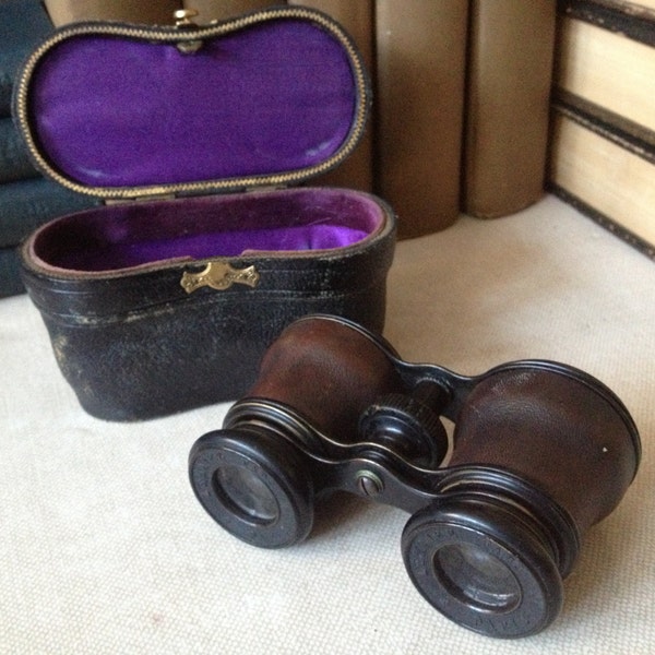 May include: Antique opera glasses with a leather covering and purple velvet lining, in a black leather case.