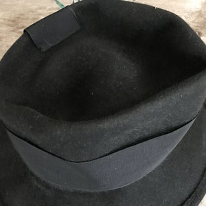 以下が含まれることがあります： つば広の黒いフェドーラハット。クラウンの周りに黒いリボンバンドが付いている。