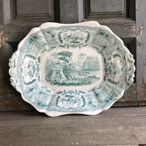May include: Vintage white and teal serving platter with a scalloped edge. The platter features a detailed pastoral scene in the centre and floral and grape vine patterns around the border. The overall design is reminiscent of vintage tableware.