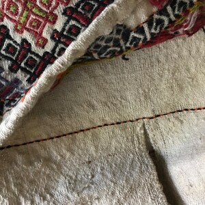 May include: Close-up of a white fabric with a black and orange stitching detail. The fabric has a woven texture and a geometric pattern.