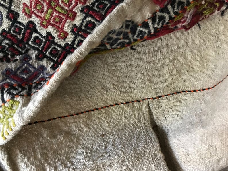 May include: Close-up of a white fabric with a black and orange stitching detail. The fabric has a woven texture and a geometric pattern.