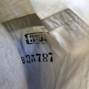 K&ouml;nnte beinhalten: Nahaufnahme eines wei&szlig;en Stoffes mit sichtbarer Naht und gestempeltem schwarzem Text. Der Text enth&auml;lt die Zahlen "3-36" in einem rechteckigen Feld und die Nummer "835787" darunter. Der Stoff scheint Teil eines Kleidungsst&uuml;cks zu sein.