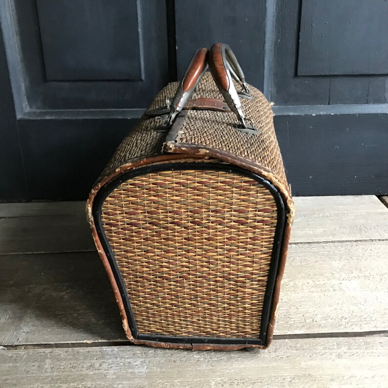 May include: A vintage woven wicker suitcase with brown leather handles and trim. The suitcase has a rounded shape and is made of natural materials.