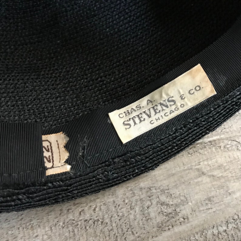 May include: A black woven hat with a black ribbon and a white label that reads "CHAS. A. STEVENS & CO. CHICAGO".